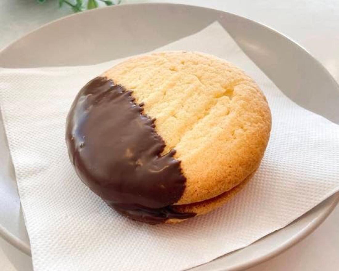 A round golden treat with one half dipped in dark chocolate, on a plate with a paper napkin