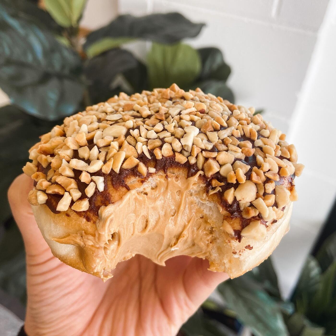 A hand holding a donut with a bite taken out, showing a creamy filling and a top covered in chopped nuts